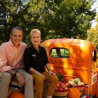 约翰和帕姆·麦维对着镜头微笑，坐在一辆橙色卡车的后座上